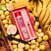 Amika x Ellis Brooklyn GUAVA GRANITA Perk Up Dry Shampoo and GUAVA GRANITA Eau de Parfum 10ml gift set lays in brown wooden bin filled with bananas, whole and sliced guavas, a bundle of vanilla beans, and almonds in a brown basket