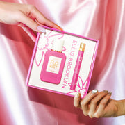 Model with nude nail polish holding top corner of Florist Eau De Parfum Gift Set Box showing Florist 50ml Eau De Parfum and Florist 10ml Eau De Parfum Travel Spray and model with grey iridescent nail polish holding bottom corner of same box, against pink satin background.