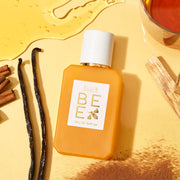 Bee 50ml Eau de Parfum sur un fond jaune clair avec du miel renversé, un verre rempli de miel, des gousses de vanille, des bâtons de cannelle, de la cannelle en poudre et des cristaux.