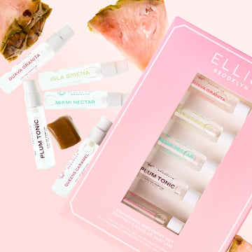Coffret de découverte des meilleures ventes à côté d'une tranche d'ananas rose, d'un cube de caramel et de flacons de 2 ml de GUAVA GRANITA Eau de Parfum, ISLA SIRENA Eau de Parfum, MIAMI NECTAR Eau de Parfum, PLUM TONIC Eau de Parfum et QUEENS CARAMEL Eau de Parfum sur un fond rose