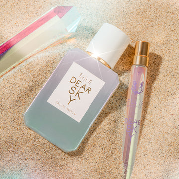 Dear Sky 50ml Eau De Parfum and Dear Sky 10ml Eau De Parfum Travel Spray slightly buried in sand next to a crystal.