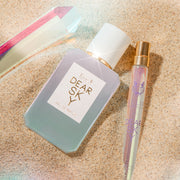 Dear Sky 50ml Eau de Parfum et Dear Sky 10ml Eau de Parfum Travel Spray légèrement enterrés dans le sable à côté d'un cristal.