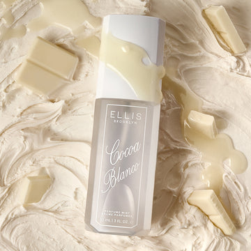 COCOA BLANCO perfume mist lays on vanilla icing, chunks of white chocolate, and a drizzle of white chocolate across the bottle.