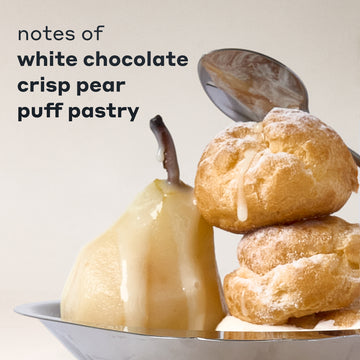 COCOA BLANCO fragrance notes displayed with a white chocolate-drizzled pear and two powdered puff pastries on a silver tray, with a spoon behind them and black text that reads 