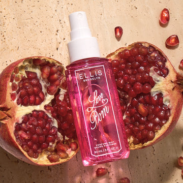 LOVE POM Perfume Mist 90ml without cap lays on two halves of a pomegranate on top of tan marble