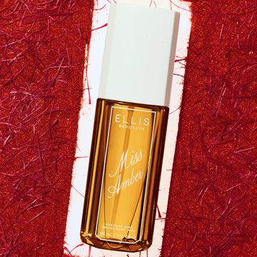Flacon de 90 mL de brume parfumée Miss Amber encadré par un fond rouge texturé.