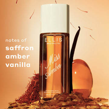 240mL Miss Amber Perfume Mist bottle standing with a vanilla bean, red saffron, and amber colored stones surrounding it with text on the left that reads 