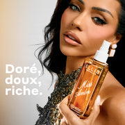 Bouteille de 240 mL de brume parfumée Miss Amber tenue par un mannequin aux cheveux foncés et portant un haut argenté orné de bijoux, sur un fond gris avec un texte à gauche qui dit « doré, doux, riche ».