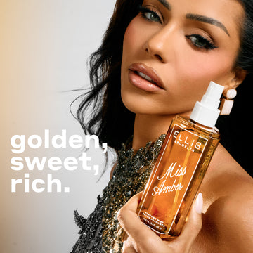 240mL bottle of Miss Amber Perfume Mist being held by a model with dark hair and a silver bejeweled top against a grey background with text on the left that reads 