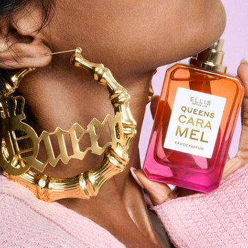 Close-up of woman wearing a pink sweater and gold hoop earrings that say 