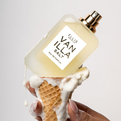 Model with nude nail polish holding ice cream cone with melted vanilla ice cream and Vanilla Salt 50ml Eau De Parfum without cap on white background. | english_image