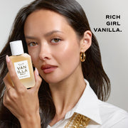 A woman with black hair wearing a white shirt, gold necklace, and gold hoop earrings holds VANILLA SALT Eau de Parfum 50ml next to her face on a gray background with black text that reads 