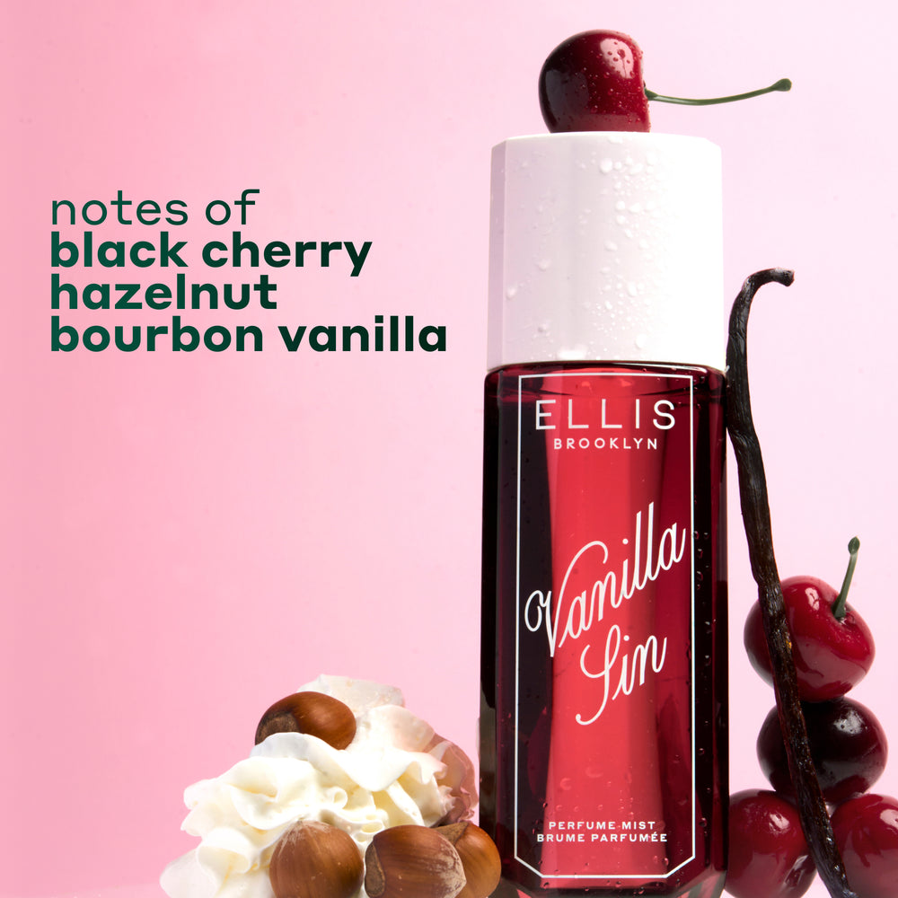 VANILLA SIN Perfume Mist 240ml topped with a cherry and between 4 stacked cherries, a vanilla bean leaning against the bottle and a pile of whipped cream with 4 hazelnuts on a pink and white ombré background with black text that reads "notes of black cherry, hazelnut, bourbon vanilla"