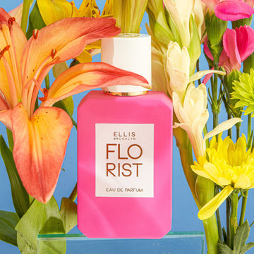Florist Eau de Parfum sur un bloc de verre contre un fond bleu entouré de fleurs roses, blanches, vertes, jaunes et orange.