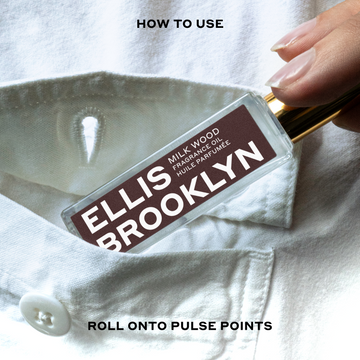 Model wearing white button-down shirt placing Milk Wood Fragrance Oil 15ml into shirt pocket between black text that reads 