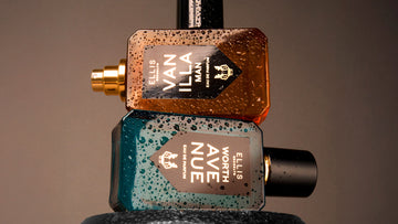 Vanilla Man 50ml Eau De Parfum with cap removed on top of Worth Avenue 50ml Eau De Pafum on top of dumbbell covered with water droplettes, on brown background.