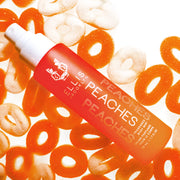 Peaches 50ml Hair and Body Fragrance Mist without cap resting on white and orange candy peach rings, on white background.