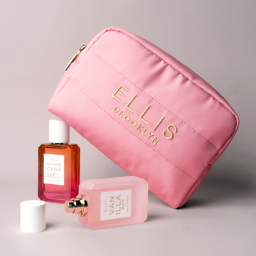 Trousse de maquillage rose avec broderie dorée indiquant « Ellis Brooklyn » posée sur QUEENS CARAMEL Eau de Parfum 50ml et derrière VANILLA RICE Eau de Parfum 50ml sans bouchon, couché à côté du bouchon sur fond gris