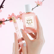Hands with pale pink manicure hold VANILLA RICE Eau de Parfum 50ml and VANILLA RICE Eau de Parfum 10ml on a pink background with pink sakura blossoms