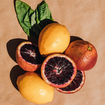 Lemons, basil, and blood oranges on textured light brown background.