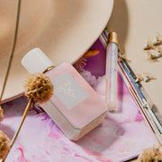 Dear Sky 50ml Eau De Parfum and Dear Sky 10ml Eau De Parfum Travel spray resting on purple and white magazine image and beige hat with dried flowers, on beige background.
