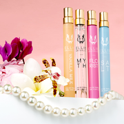 Vanilla Milk 10ml Eau De Parfum Travel Spray, Myth 10ml Eau De Parfum Travel Spray, Florist 10ml Eau De Parfum Travel Spray, and Salt 10ml Eau De Parfum Travel Spray on white table next to white, purple, pink, white, and yellow flowers, and string on pearls, on light pink background.
