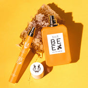 Bee 10ml Eau De Parfum travel Spray with cap removed and Bee 50ml Eau De Parfum with cap removed resting on piece of honeycomb, on yellow background.