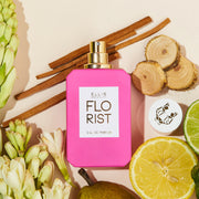 Florist 50ml Eau De Parfum with cap removed on pale pink background with lemon, lime, sandal wood, pear, flowers, and cedar wood.
