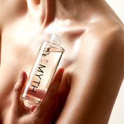 Model holding Myth Spectacular Scented Body Oil 95ml with cap removed near chest on white background.