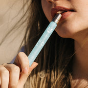 Model with blonde hair holding Salt 10ml Eau De Parfum Travel Spray to lower lip against beige background.